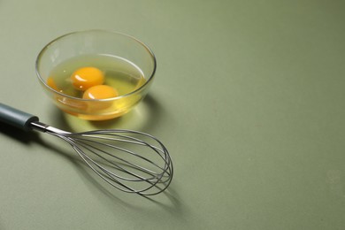 Photo of Metal whisk and raw eggs in bowl on khaki background. Space for text