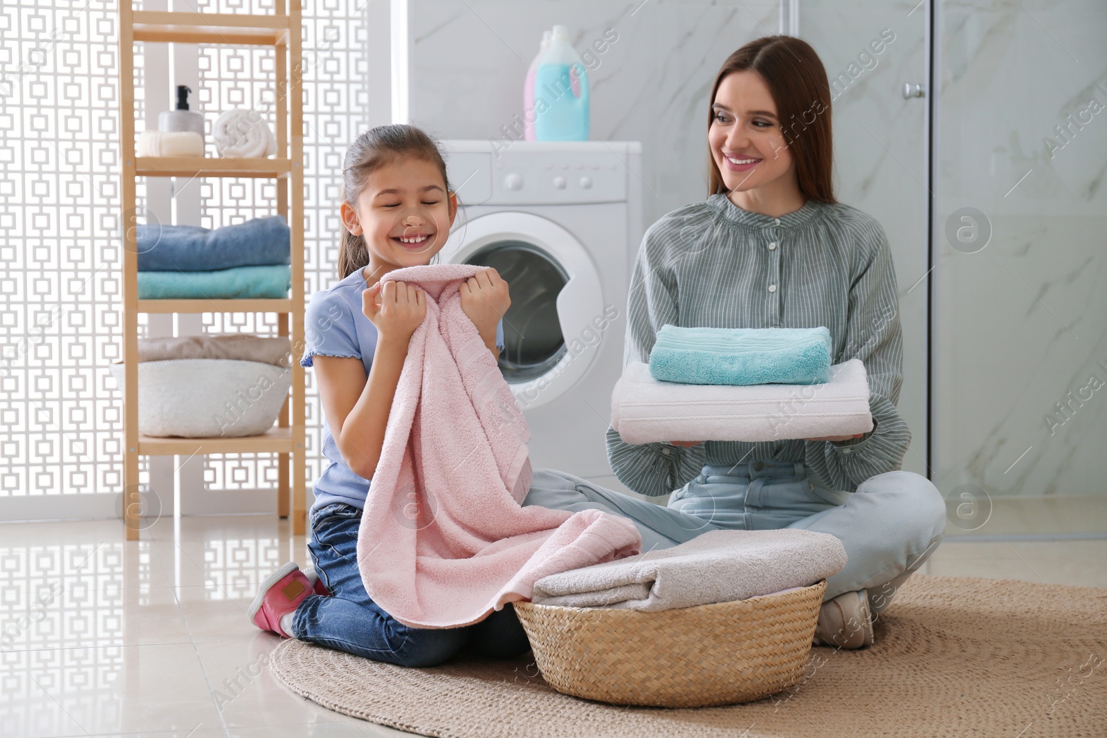 Photo of Mother and little daughter with clean laundry in bathroom