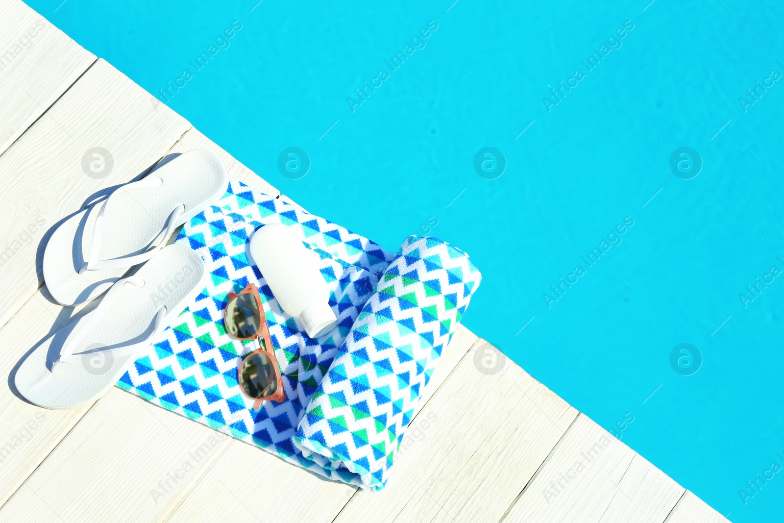 Photo of Beach accessories on wooden deck near swimming pool, top view. Space for text