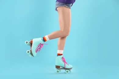 Young woman with retro roller skates on color background, closeup