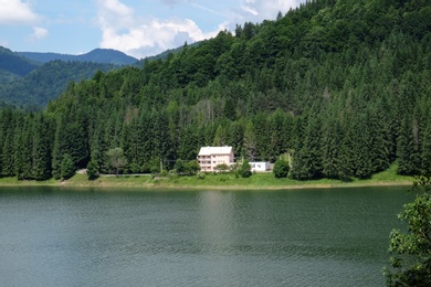 Lonely house in green forest at bottom of hill near lake