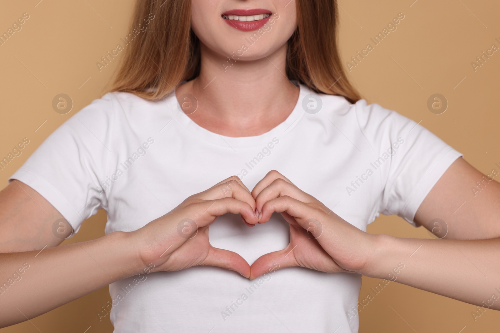Photo of Young woman making heart with hands on beige background, closeup. Volunteer concept
