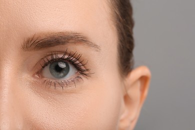 Woman with long eyelashes after mascara applying against grey background, closeup