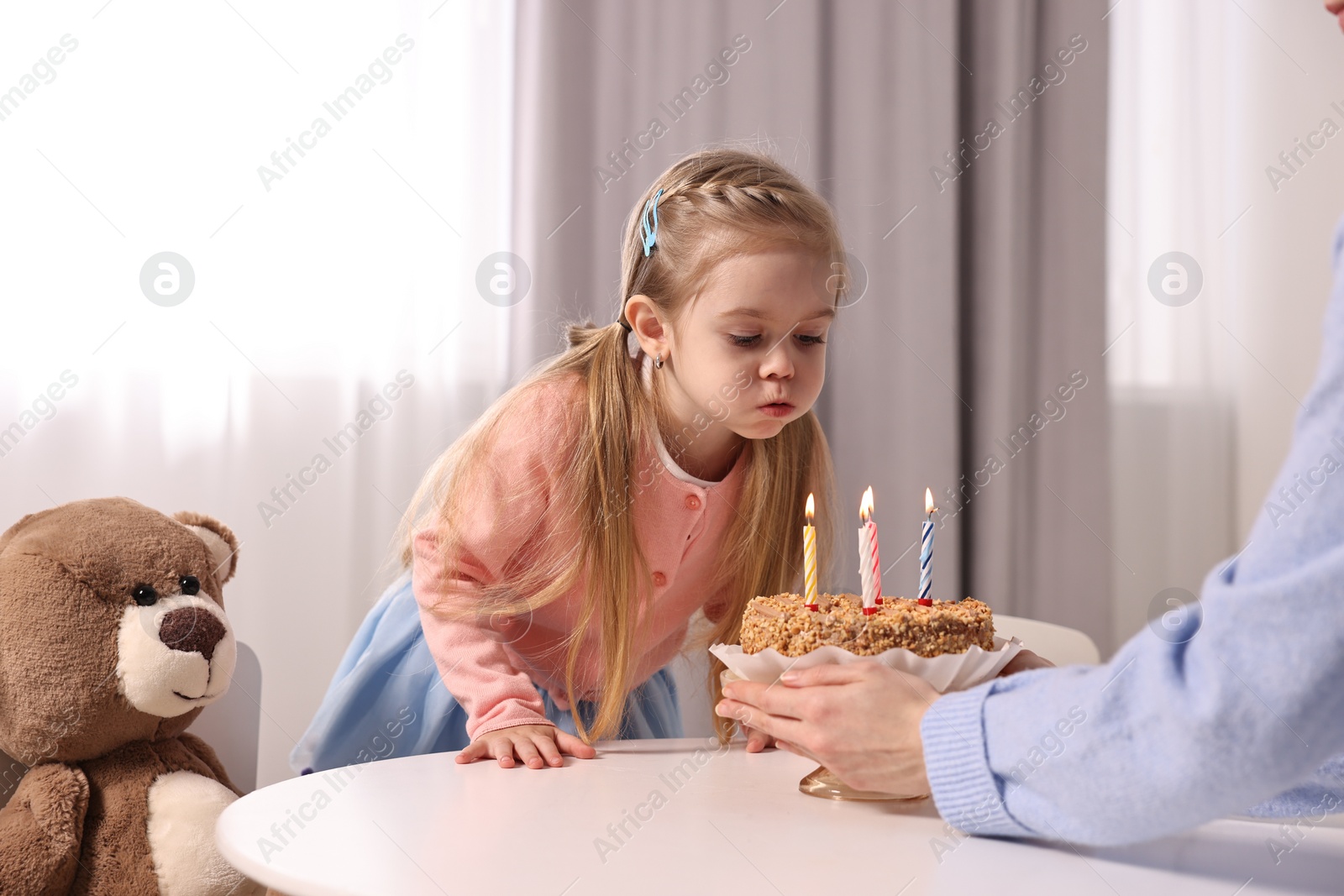 Photo of Birthday celebration. Mother holding tasty cake with burning candles near her daughter indoors