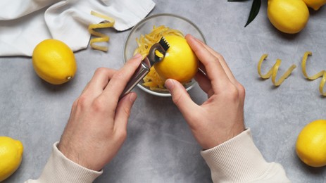 Photo of Man zesting lemon at grey table, closeup