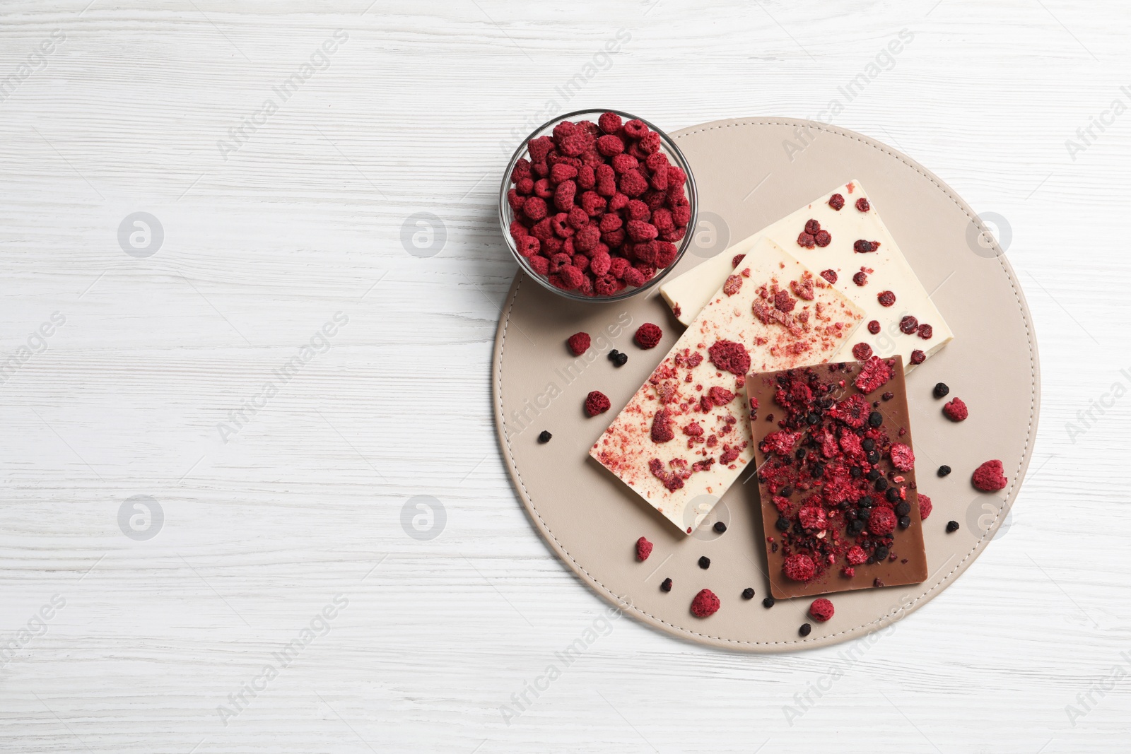 Photo of Chocolate bars with freeze dried fruits on white wooden table, top view. Space for text