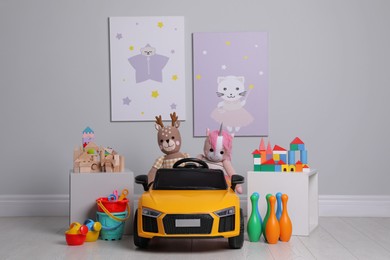 Child's electric car with other toys near light wall in play room