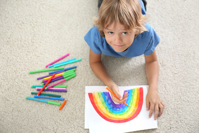 Photo of Little boy drawing rainbow on floor indoors, above view. Stay at home concept