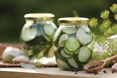 Photo of Jars of delicious pickled cucumbers and ingredients on wooden table against blurred background, closeup. Space for text
