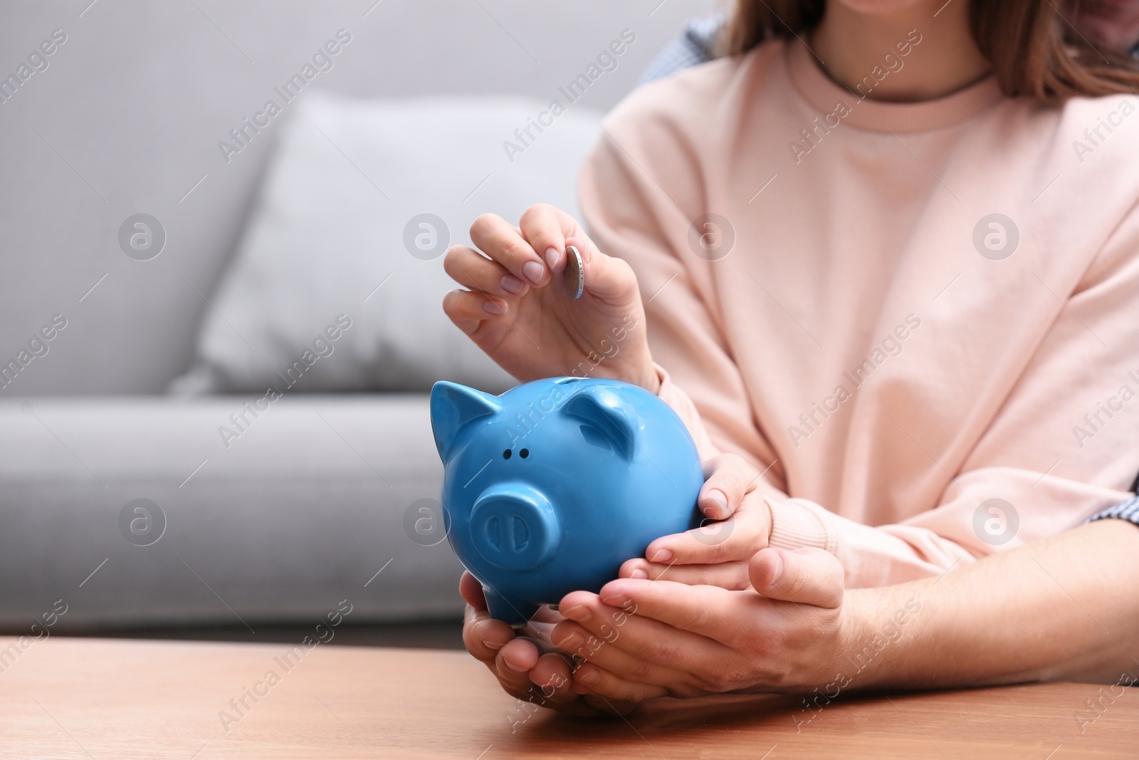 Photo of Couple with piggy bank and coin at wooden table, closeup