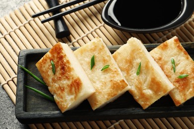 Delicious turnip cake with green onion and soy sauce on grey table, closeup