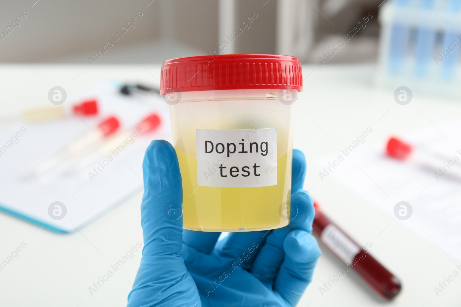Photo of Doctor holding jar with urine sample indoors, closeup. Doping control