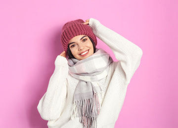 Young woman wearing warm sweater, scarf and hat on pink background. Winter season