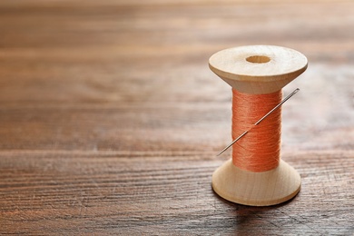 Photo of Spool of thread with needle on wooden background. Tailoring equipment