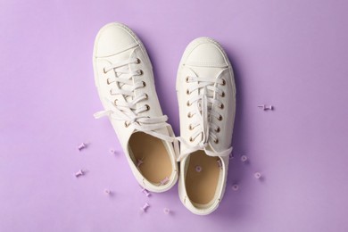 Photo of Sneakers with pins on violet background, flat lay. Celebrating April Fool's day