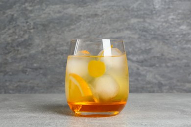 Photo of Delicious cocktail with orange, yellow cherry and ice balls on grey table