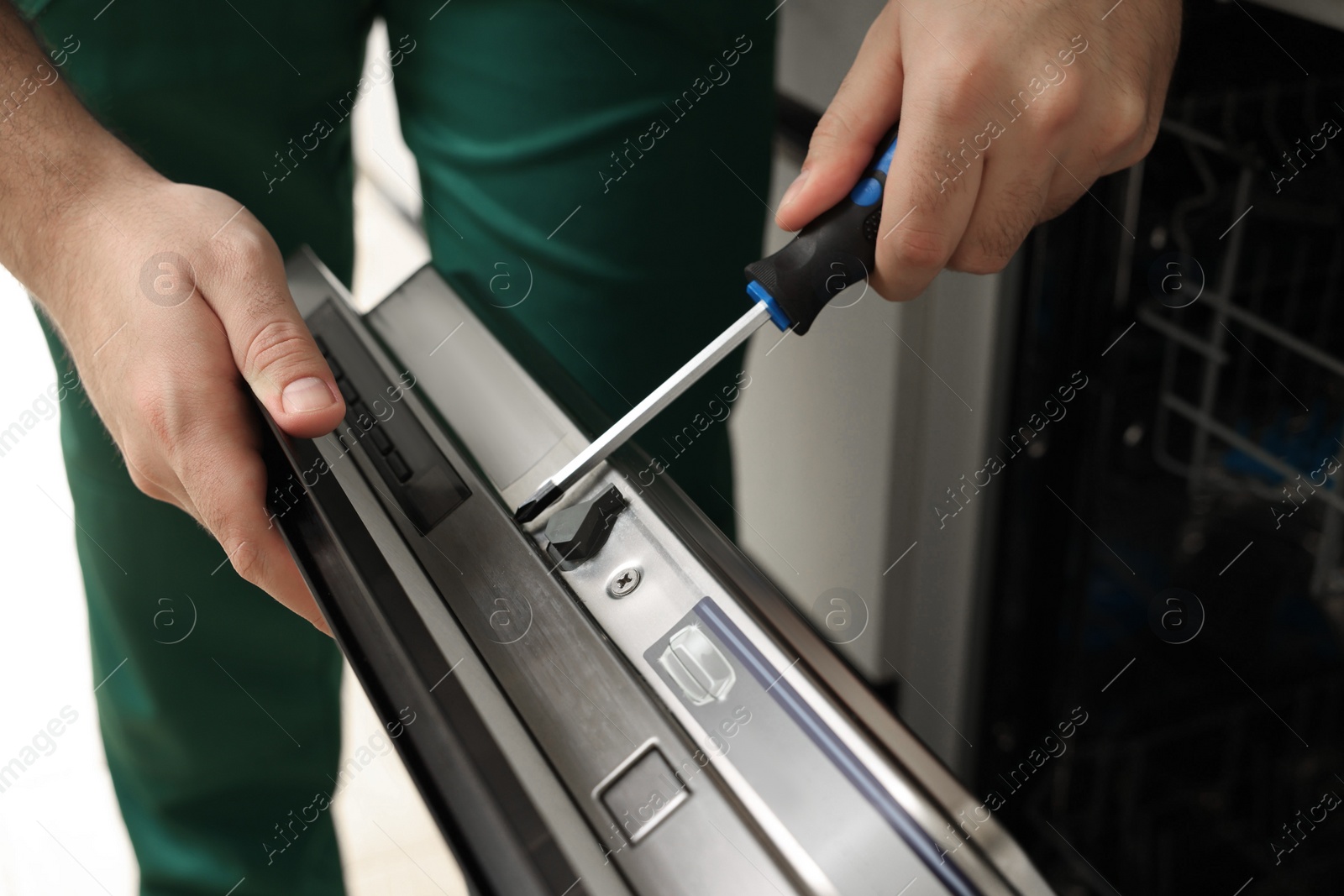 Photo of Serviceman repairing dishwasher door with screwdriver indoors, closeup