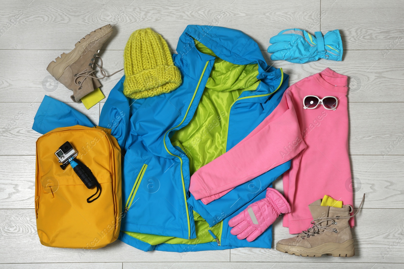 Photo of Set of warm clothes and action camera on wooden background, flat lay. Winter vacation