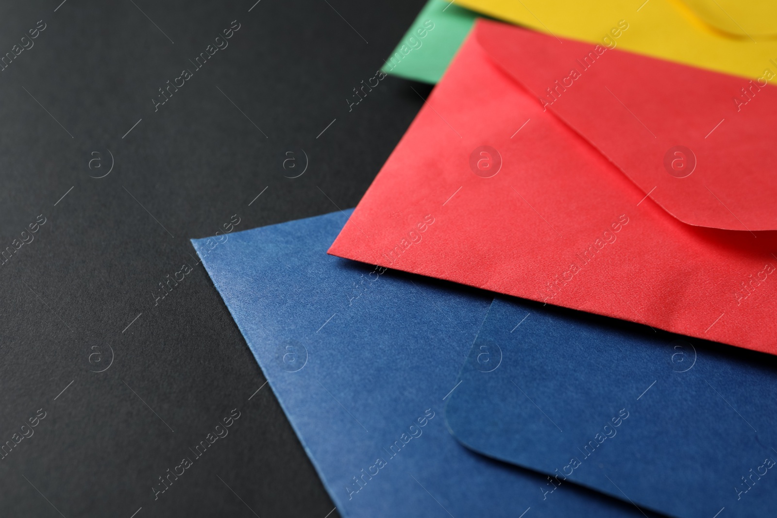 Photo of Colorful paper envelopes on black background, closeup