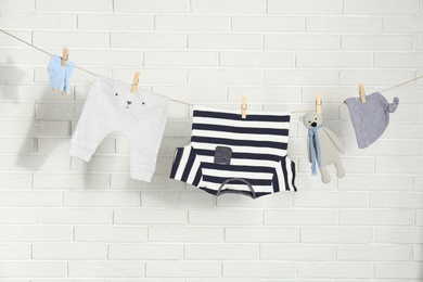 Baby clothes hanging on washing line near white brick wall