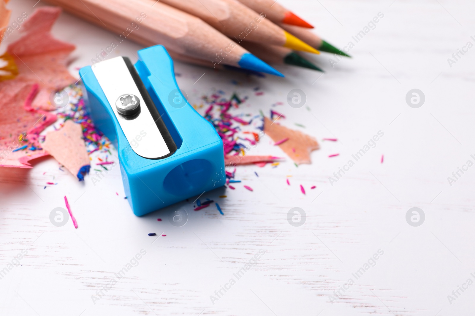 Photo of Colorful pencils, sharpener and shavings on white wooden background, closeup