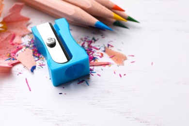 Photo of Colorful pencils, sharpener and shavings on white wooden background, closeup