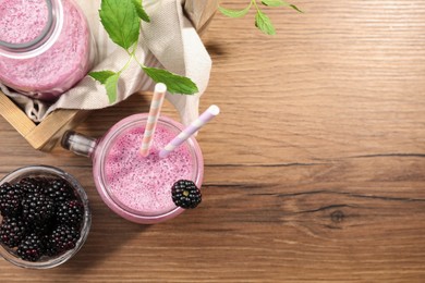 Different glassware of delicious blackberry smoothie and fresh berries on wooden table, flat lay. Space for text