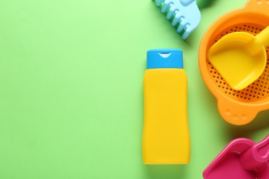 Bottle of suntan cream and children's beach toys on light green background, flat lay. Space for text