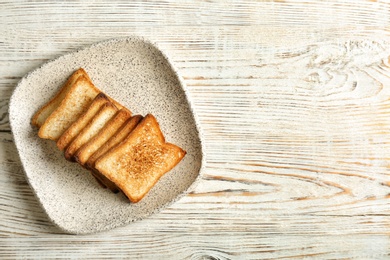 Plate with toasted bread on wooden background, top view