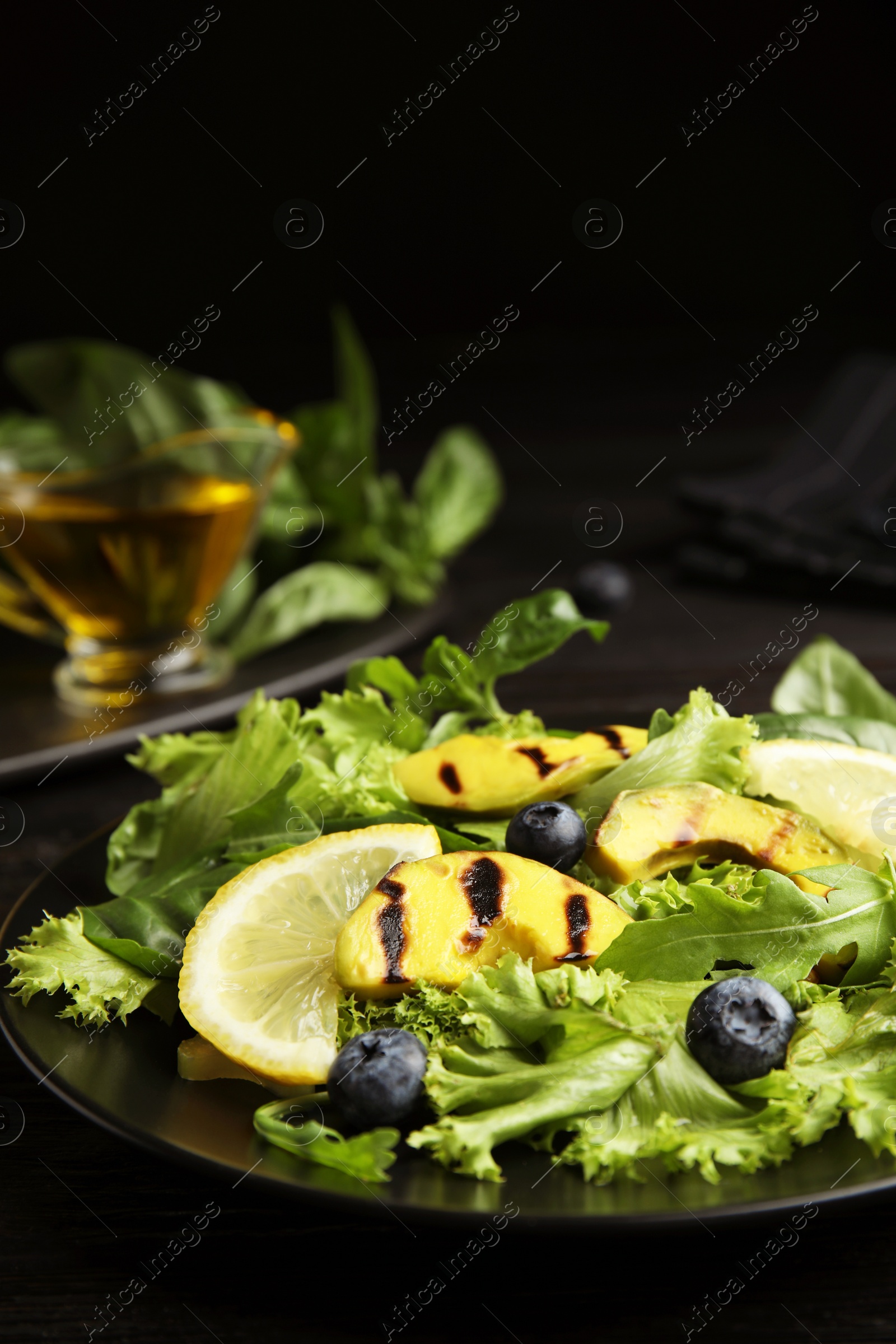 Photo of Delicious avocado salad with lemon and blueberries on black table