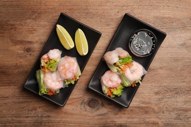 Photo of Tasty spring rolls served with lime and soy sauce on wooden table, flat lay