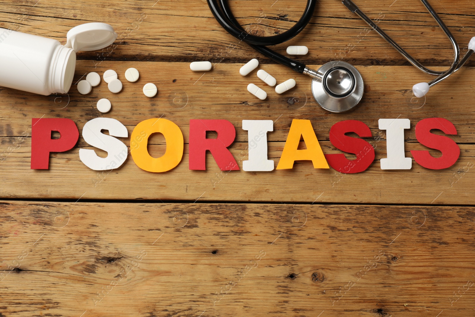 Photo of Word Psoriasis made of paper letters, stethoscope and pills on wooden table, flat lay. Space for text