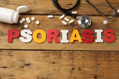 Photo of Word Psoriasis made of paper letters, stethoscope and pills on wooden table, flat lay. Space for text