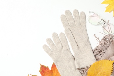 Photo of Stylish woolen gloves, scarf, glasses and dry leaves on white background, top view