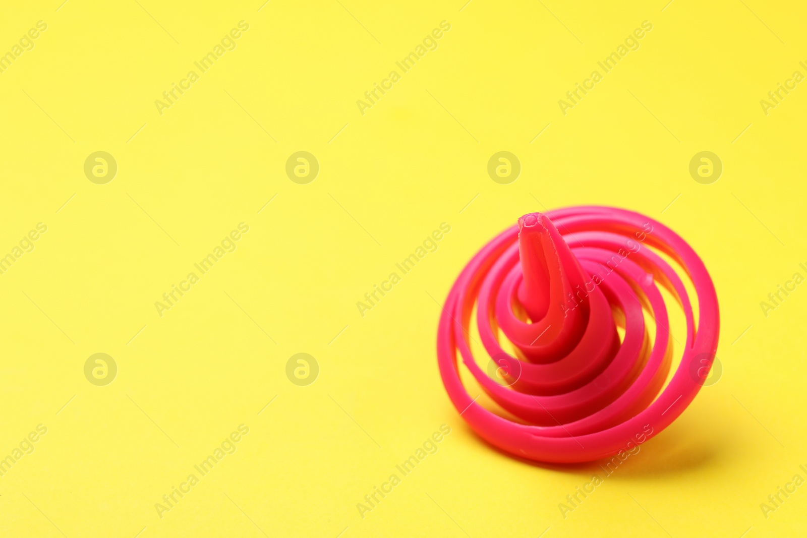 Photo of One pink spinning top on yellow background, closeup. Space for text