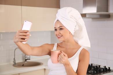 Photo of Beautiful woman with towel on head taking selfie in kitchen