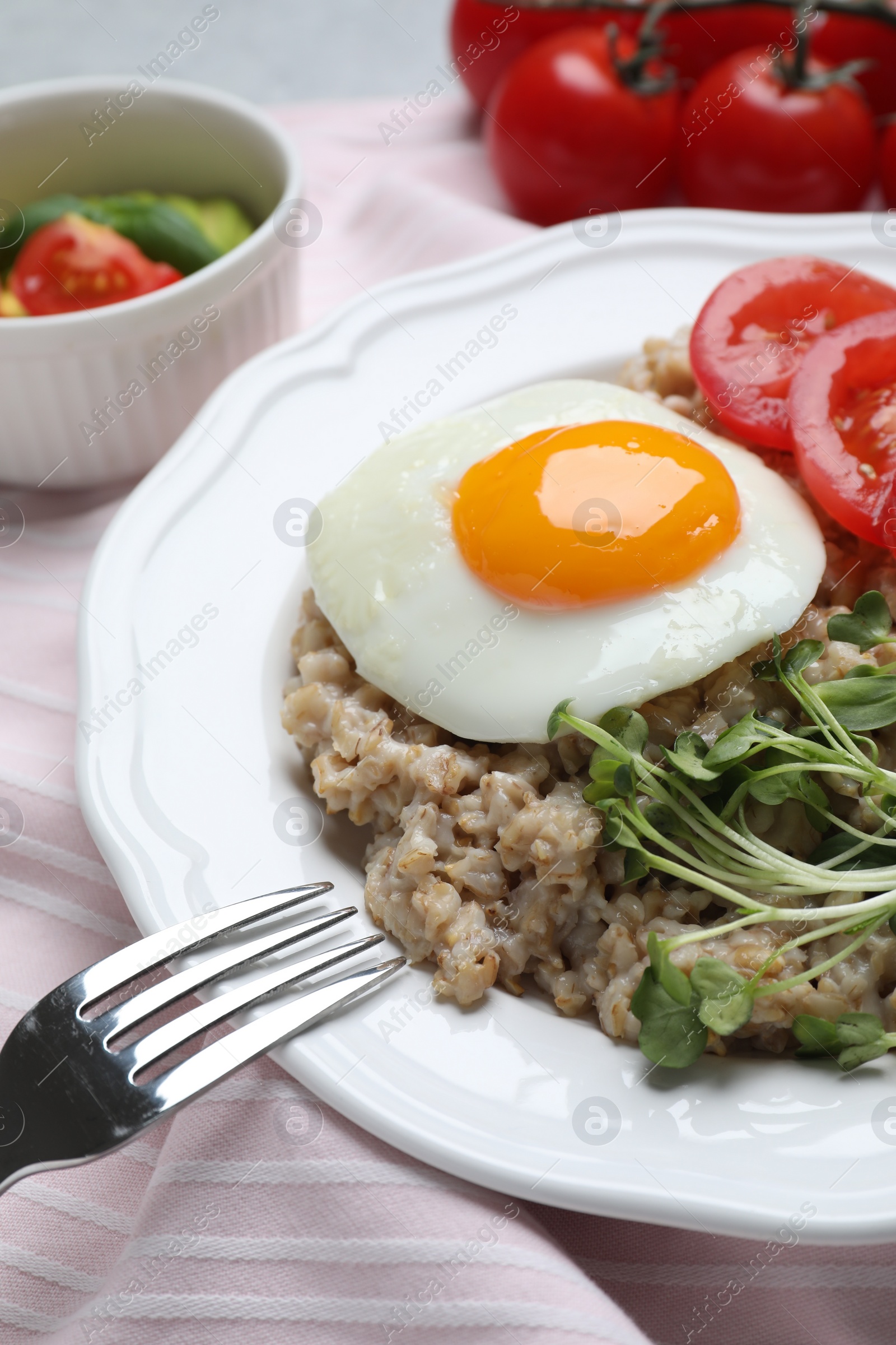 Photo of Delicious boiled oatmeal with fried egg, tomato and microgreens on table, closeup