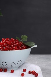 Ripe red currants and leaves in colander on grey textured table. Space for text