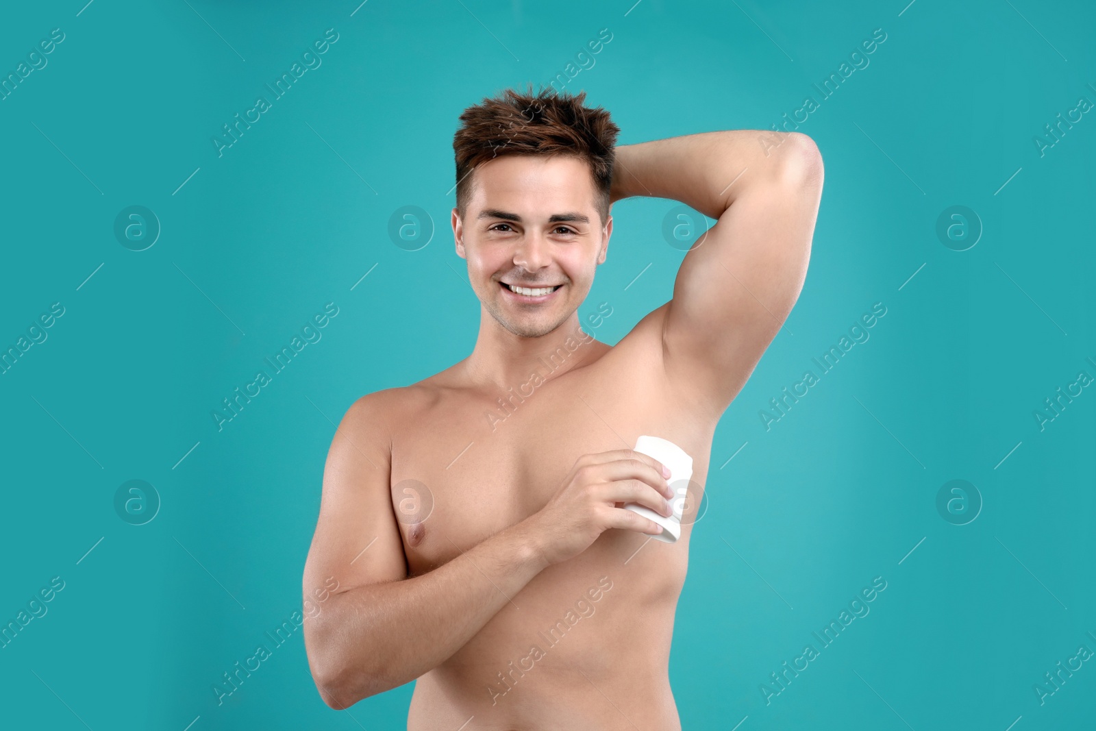 Photo of Young man applying deodorant to armpit on blue background