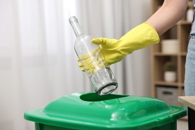 Photo of Garbage sorting. Woman throwing glass bottle into trash bin in room, closeup