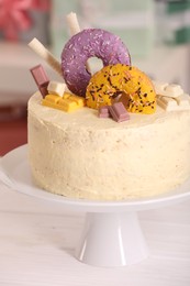 Photo of Delicious cake decorated with sweets and balloons on white wooden table, closeup