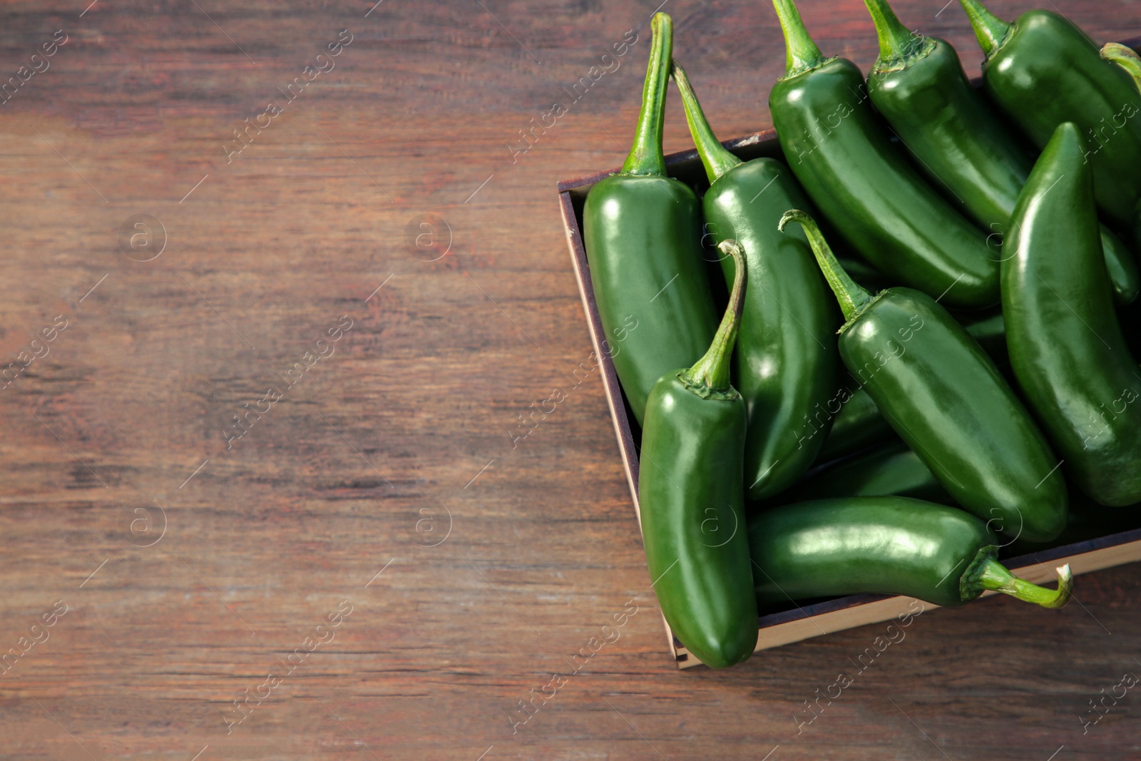 Photo of Crate with green jalapeno peppers on wooden table, top view. Space for text