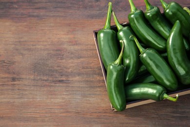 Photo of Crate with green jalapeno peppers on wooden table, top view. Space for text