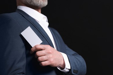 Photo of Businessman holding blank business card on black background, closeup. Space for text