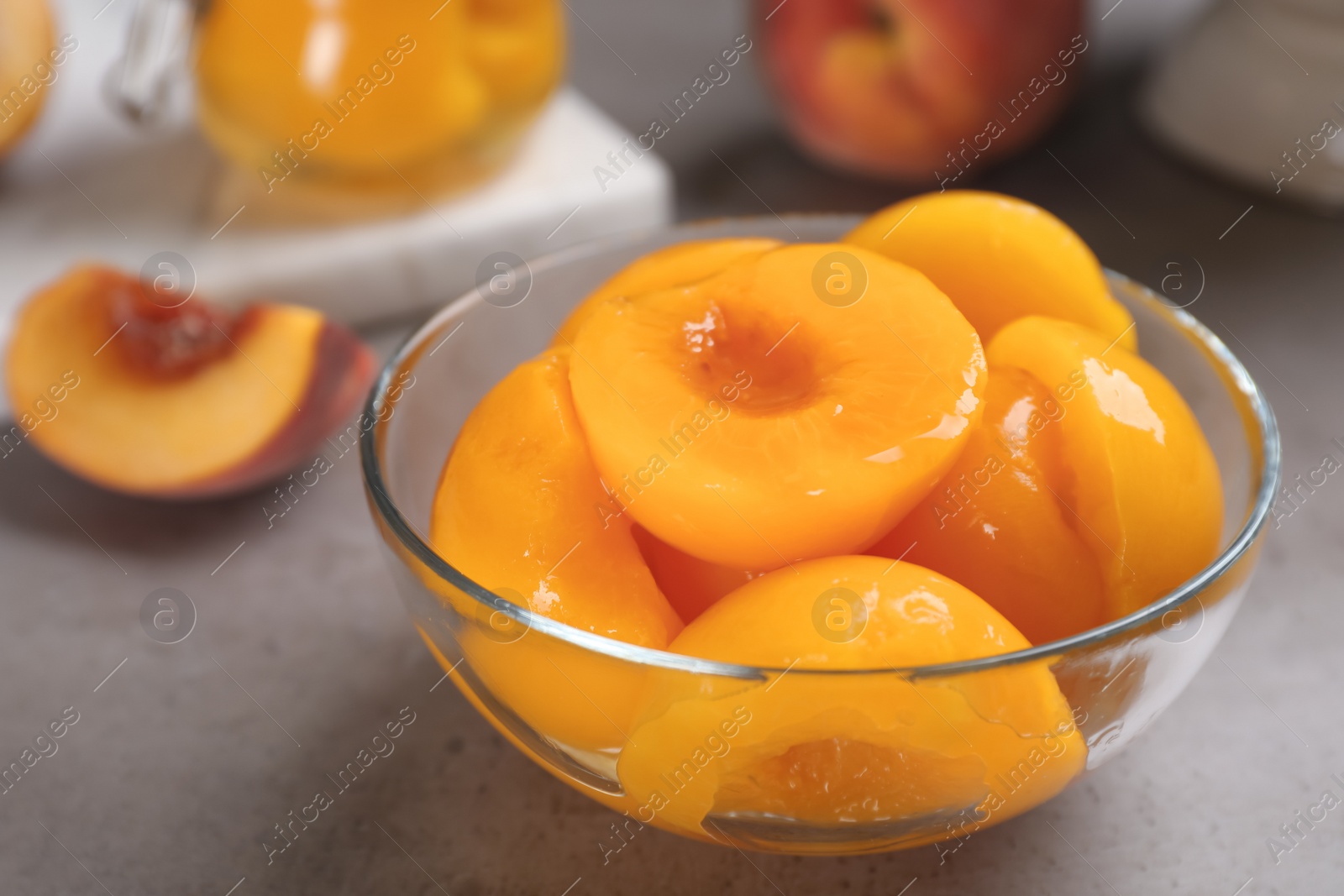 Photo of Glass bowl with conserved peach halves on grey table