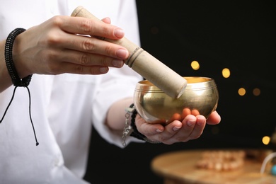 Photo of Woman using singing bowl in sound healing therapy on black background, closeup