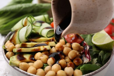 Pouring balsamic vinegar onto delicious salad with chickpeas and vegetables, closeup
