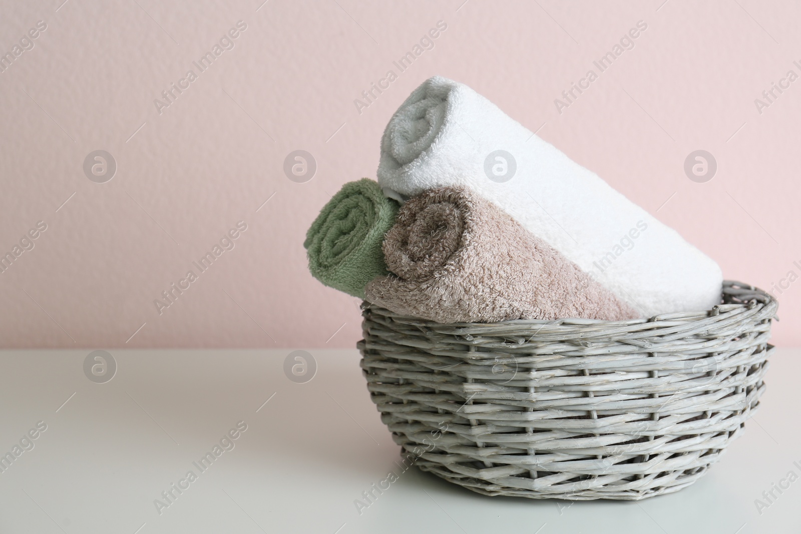 Photo of Wicker basket with clean soft towels on grey table near pink wall. Space for text