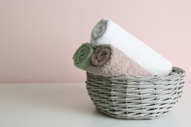 Photo of Wicker basket with clean soft towels on grey table near pink wall. Space for text