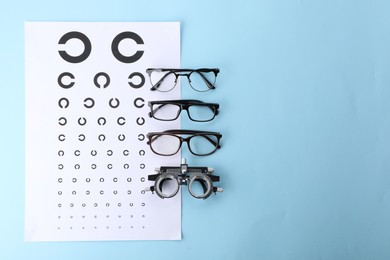Photo of Vision test chart, glasses and trial frame on light blue background, flat lay. Space for text
